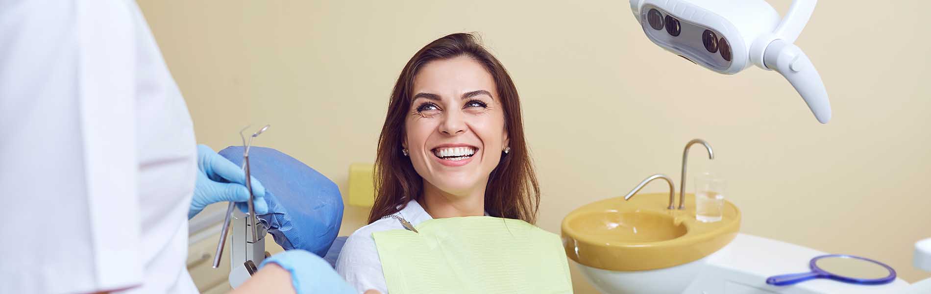 A person is seated in a dental chair, receiving care from a dental professional who stands behind them.